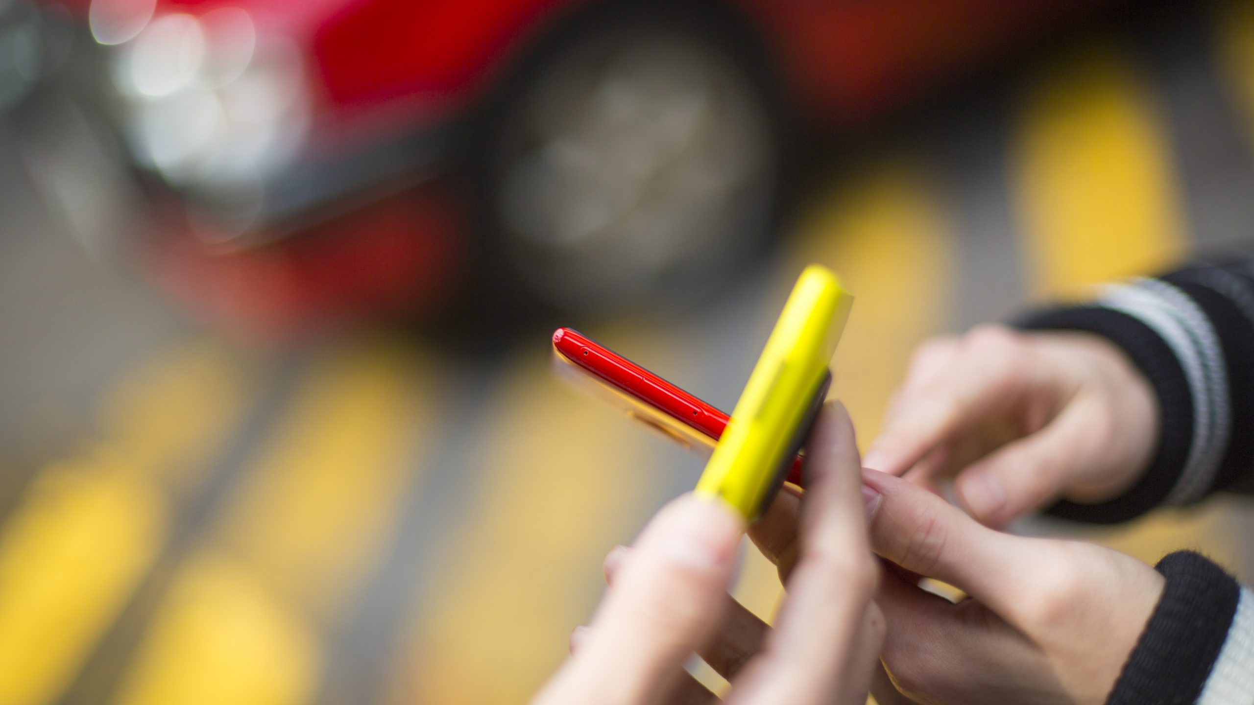 Yellow and red smartphones with blurred yellow and red background on the street. Photographer Tuomas Harjumaaskola.