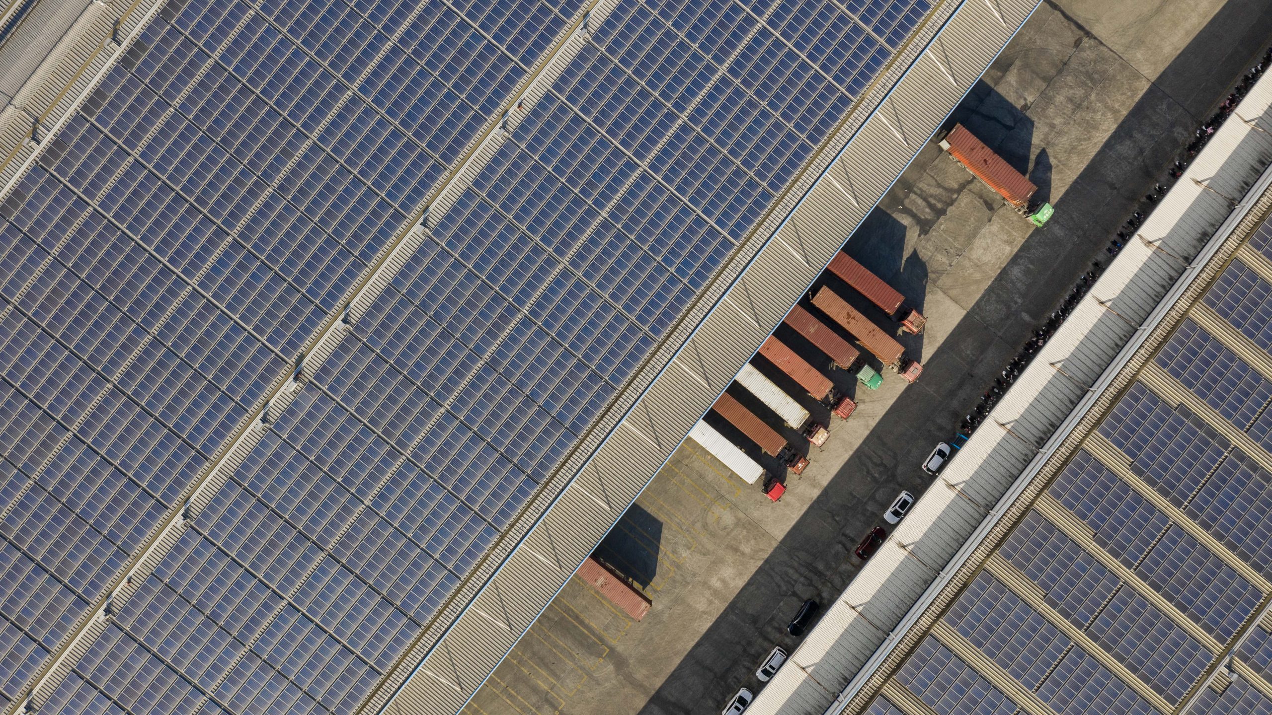 Drone photography China, factory roof filled with solar panels, trucks underneath. Photographer Tuomas Harjumaaskola.