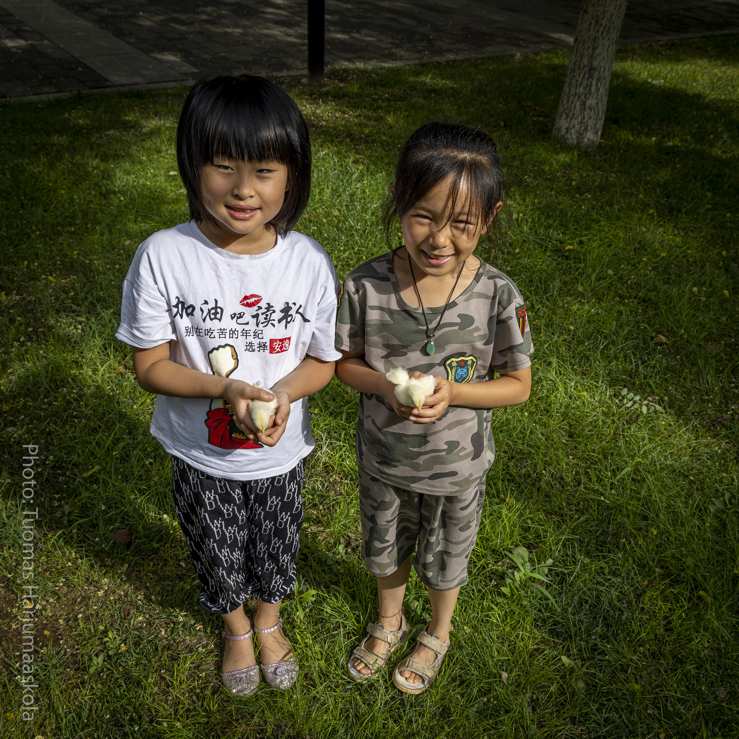 Two Chinese girls holding chicks in their hands at a park. Photographer Tuomas Harjumaaskola.