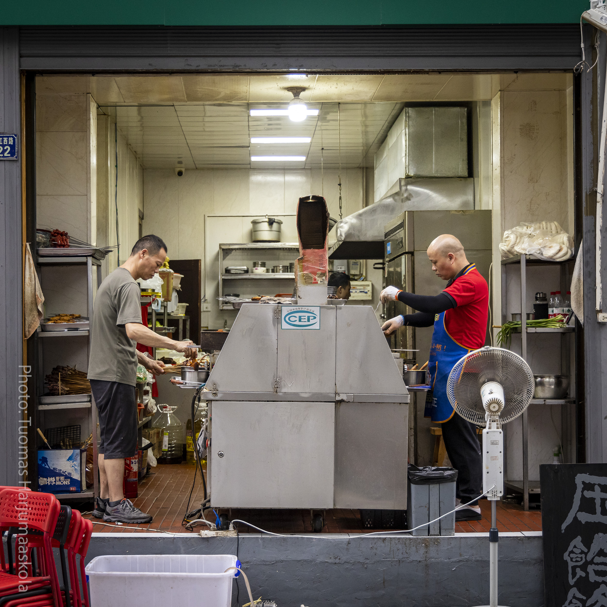 Chinese restaurant’s kitchen, view from street, two chefs cooking. Photographer Tuomas Harjumaaskola.