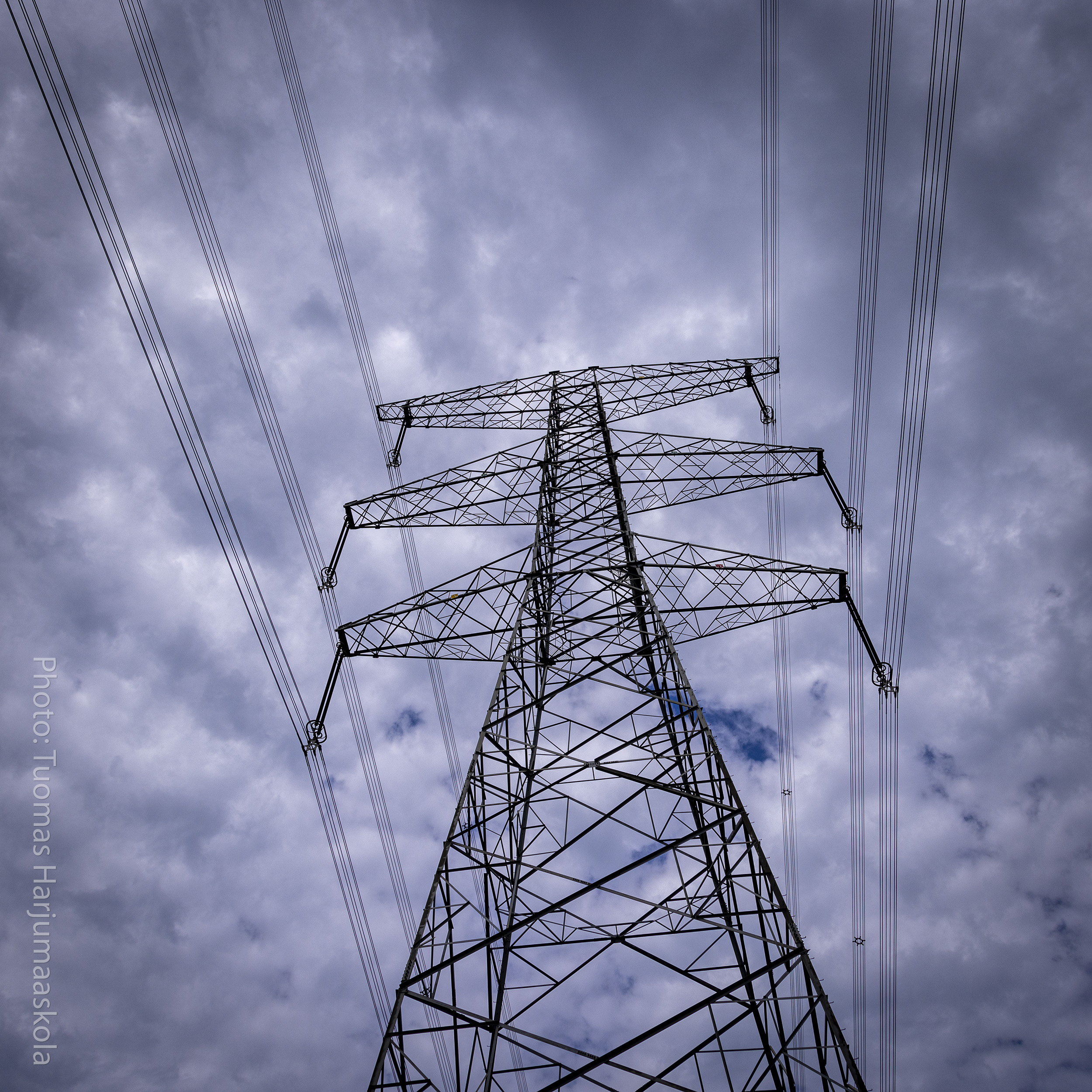 A transmission tower photographed from underneath, heavy clouds hanging above. Photographer by Tuomas Harjumaaskola.
