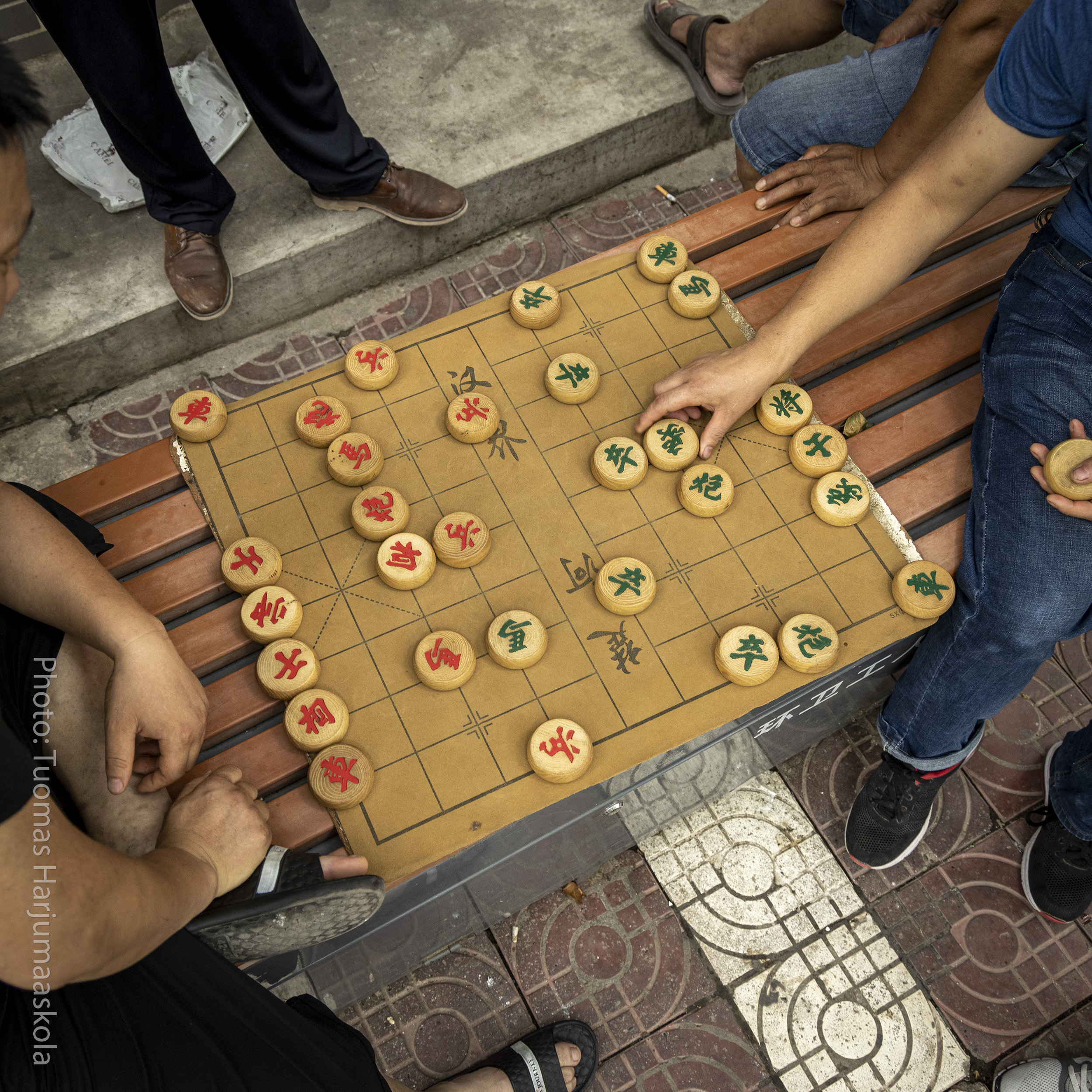 A group of men playing Chinese chess, xiangqi, on the sidewalk. Photographer by Tuomas Harjumaaskola.
